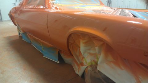 1973 Chevrolet Camaro - The side of an orange 1973 Chevrolet Camaro is shown as it undergoes a paint job, with masking tape and plastic covering the wheels and low…