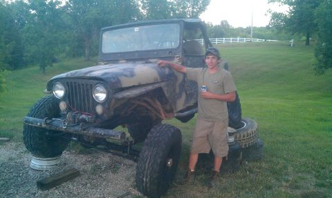 1987 Ford Bronco - Person stands next to a heavily modified Jeep CJ with oversized tires and camouflage paint.