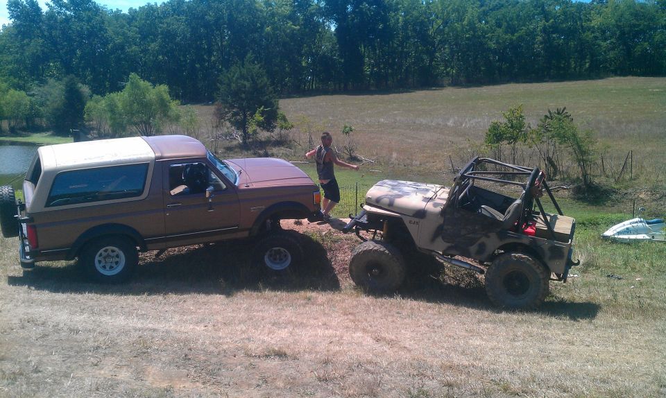Brown Ford Bronco being towed by a lifted Jeep off-road. Person standing between them