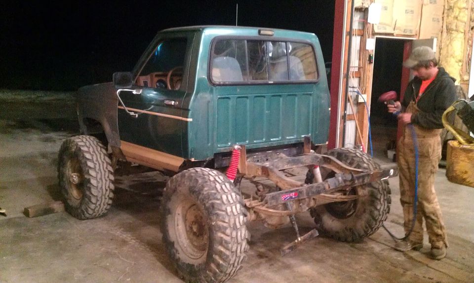 Green Ford Bronco with large tires and exposed frame, undergoing modification