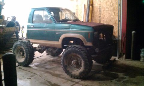 1987 Ford Bronco - This lifted pickup truck features large off-road tires and two-tone green and tan paint.