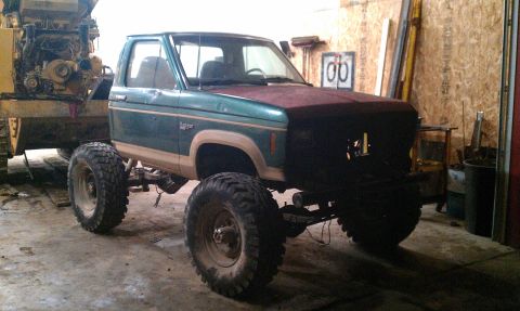 1987 Ford Bronco - This modified pickup truck is parked indoors next to some industrial machinery.