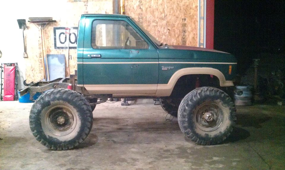 Green Ford Ranger pickup truck with large tires and lifted suspension, missing its bed