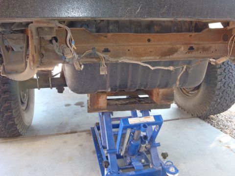1978 Ford Bronco - The fuel tank of a vehicle is shown supported by a blue hydraulic jack, revealing the undercarriage components.