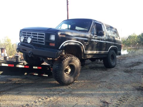 1986 Ford Bronco - A lifted black Ford Bronco is positioned on a trailer, ready for transport.