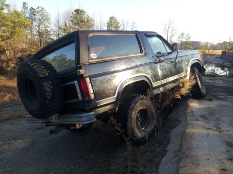 1986 Ford Bronco - 1986 Ford Bronco navigating rough terrain with its rear-mounted spare tire visible.