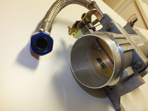 2003 Ford Crown Victoria - Angled view of a throttle body bolted to an aluminum intake elbow with a braided hose and blue anodized end fitting.