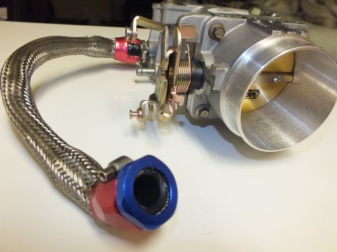 2003 Ford Crown Victoria - Angled shot of a throttle body with open bore, linkage and a braided hose ending in blue and red anodized fittings.