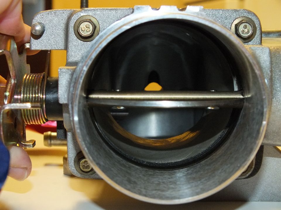 Throttle body bore interior with throttle plate horizontal and mounting screws around flange