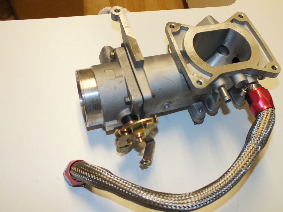 Aluminum intake manifold and throttle body unit with braided hose and red AN fittings on white surface