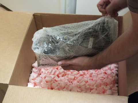 2003 Ford Crown Victoria - bubble-wrapped metallic part held over an open shipping carton lined with pink foam peanuts