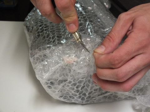 2003 Ford Crown Victoria - Scissors snip through bubble-wrap packaging held by two hands at a desk.
