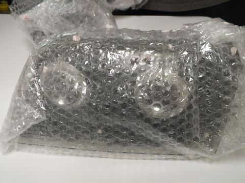 2003 Ford Crown Victoria - Two clear headlight lenses remain sealed inside bubble-wrap bags on a white surface.