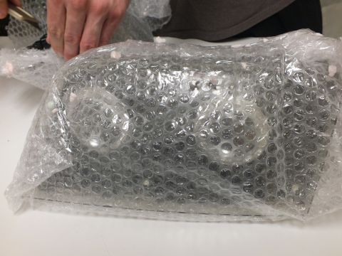 2003 Ford Crown Victoria - clear lens component packaged in bubble wrap rests on a desk beside another bag.