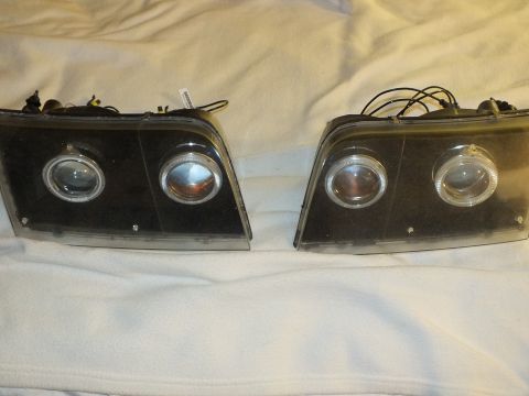 2003 Ford Crown Victoria - Left and right black projector halo headlights with attached HID wiring laid side by side.