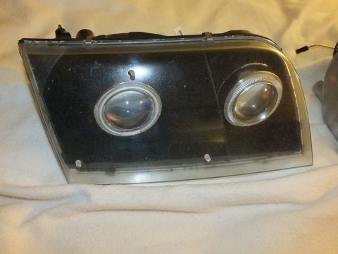 2003 Ford Crown Victoria - smoked black projector and halo headlight unit photographed on a soft surface.