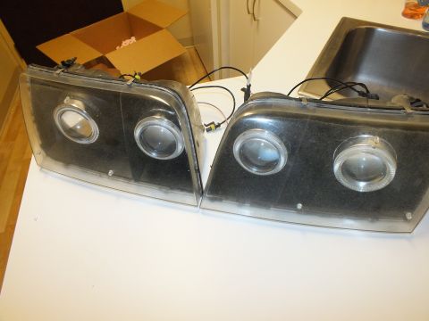 2003 Ford Crown Victoria - Two black dual-projector halo headlights set on a counter beside an open box and sink.
