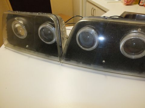 2003 Ford Crown Victoria - left and right pair of smoked projector halo headlights with trailing wiring on a counter.