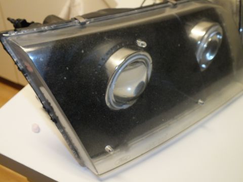 2003 Ford Crown Victoria - Angled view of a smoked black projector headlight with twin lenses and a Ford oval mark.