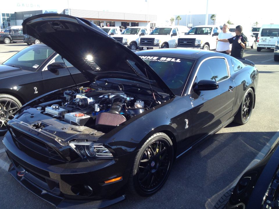 Black Ford Mustang with hood open, showing engine, custom black wheels, and a "NNE BELL" sticker on windshield