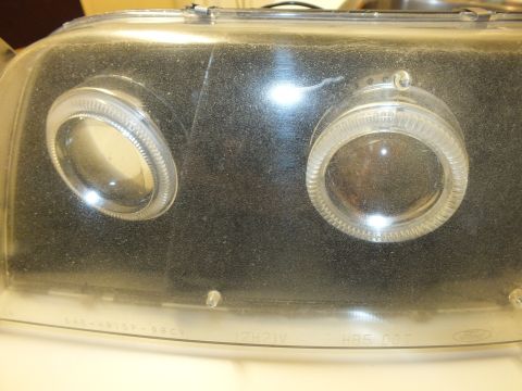 2003 Ford Crown Victoria - Detail of a smoked projector headlight showing twin halo lenses and SAE-HR15P-98CV marking.
