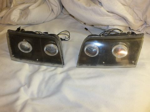 2003 Ford Crown Victoria - Two retrofit headlights, each with twin projector lenses, halo rings and wiring pigtails, laid out for comparison.