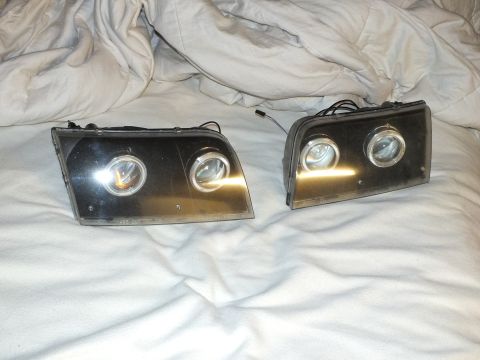 2003 Ford Crown Victoria - Retrofit dual-projector headlamp pair, halo rings and connectors visible against light glare.