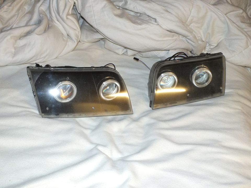Two custom projector headlight assemblies with glare-reflected lenses on white bedding
