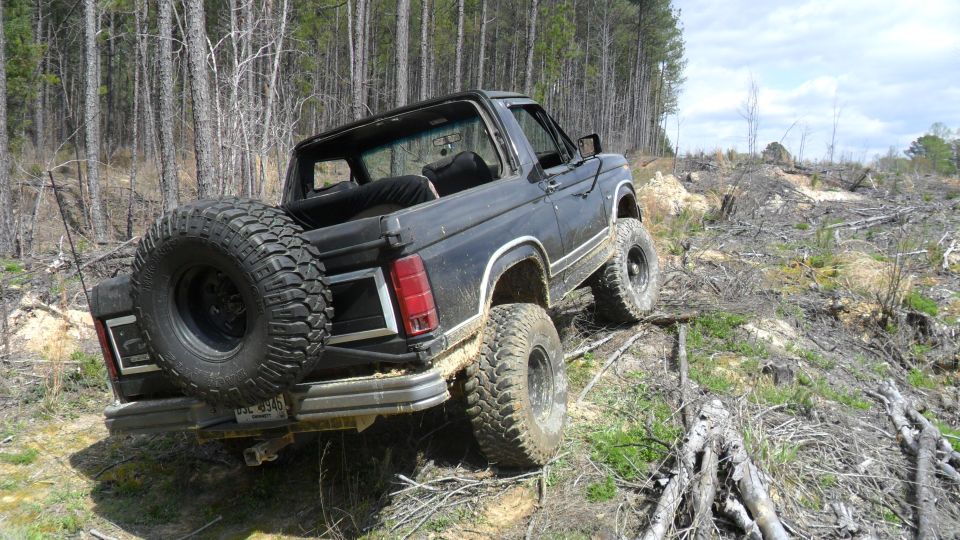 1986 Ford Bronco with large tires on a muddy, wooded hill
