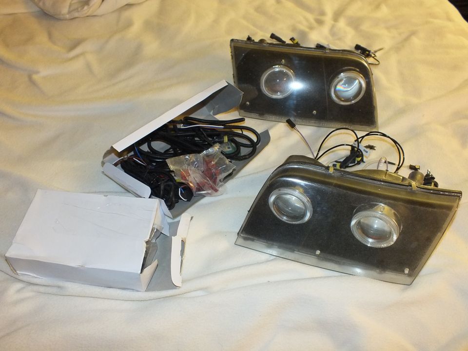 Two dual-projector headlights with white box of HID wiring kit on white bedding