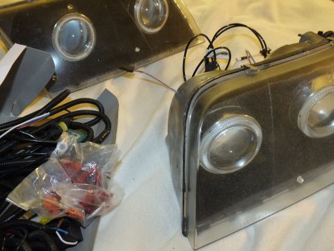 2003 Ford Crown Victoria - Detail of a halo projector headlight beside its chrome reflector plate and a bag of red wiring components.