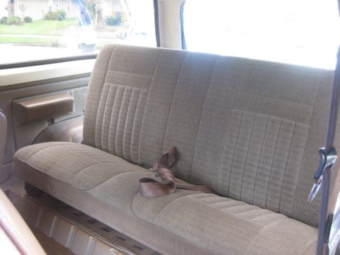 1994 Ford Bronco - The interior of a vehicle shows a rear bench seat with brown fabric upholstery and a seatbelt.