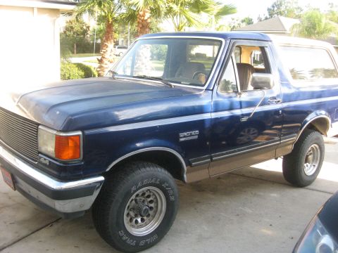 1994 Ford Bronco - This 1992 Ford Bronco is blue with tan trim and chrome wheels, seen from the front-three-quarter view.