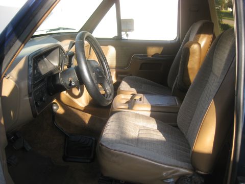 1994 Ford Bronco - The interior of this Ford Bronco features cloth seats and a tan dashboard with a prominent steering wheel.