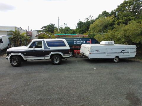 1984 Ford Bronco - A Ford Bronco tows a pop-up camper, with a service van visible behind it.