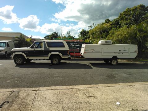 1984 Ford Bronco - Ford Bronco towing a pop-up camper trailer on a street.