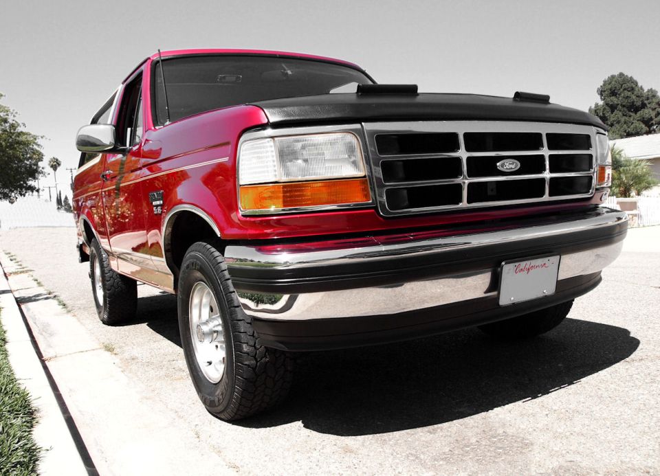 Red Ford Bronco low front three-quarter view with black hood bra and chrome grille