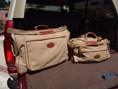 1994 Ford Bronco - Matching tan canvas luggage with brown leather trim and oval logo patches sitting on the carpeted rear cargo floor of a red SUV with the ta…