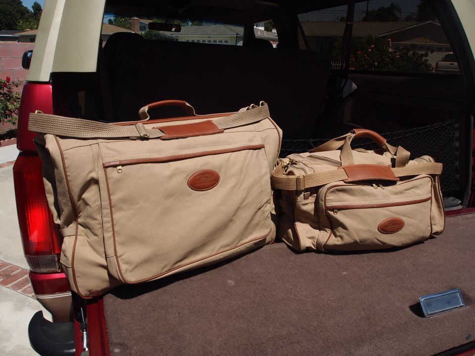 Tan canvas luggage set on the carpeted cargo floor of a red SUV, tailgate down