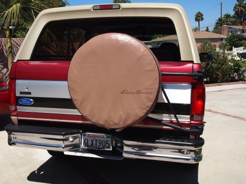 1994 Ford Bronco - Straight-on rear view of a red Ford Bronco with a white removable hardtop, showing a tan "Eddie Bauer" spare tire cover on a swing-out carr…