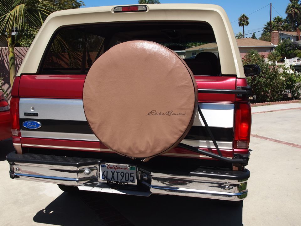 Rear of red and white Ford Bronco with tan Eddie Bauer spare tire cover and California plate