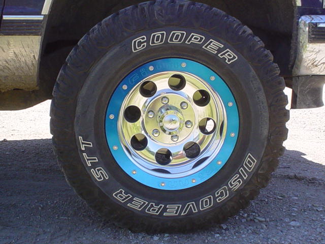 Close-up of a Cooper Discoverer STT tire on a chrome rim with a blue accent ring
