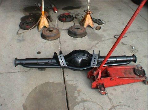 1979 Ford Bronco - Rear axle assembly and brake components laid out on concrete floor with jack stands and floor jack.