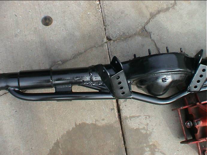 Black-painted rear axle housing with welded truss and multi-hole link brackets on concrete