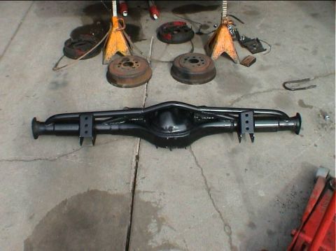 1979 Ford Bronco - A black rear axle assembly is laid out on a concrete surface, with brake drums and jack stands visible.
