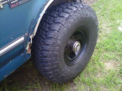 1994 Ford Bronco - Close-up of a teal SUV's fender and a large off-road tire, showing some rust damage.