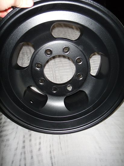 1994 Ford Bronco - A black wheel with a matte finish is shown, with a hand visible at the top edge.