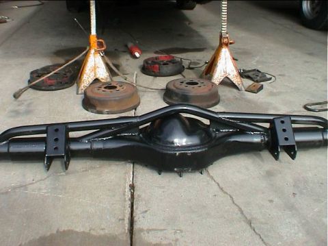 1979 Ford Bronco - A freshly painted rear axle assembly sits on a concrete surface with brake drums and jack stands nearby.