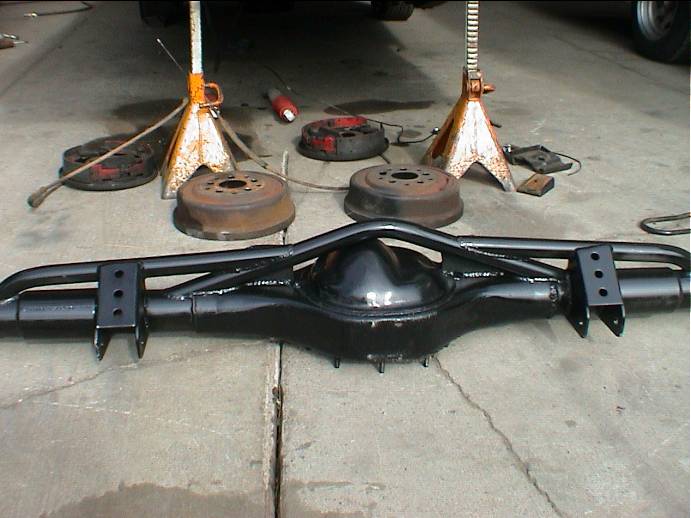Black-painted rear axle housing with four-link brackets on a garage floor