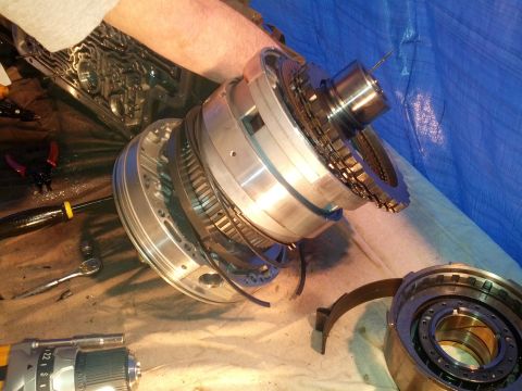 1995 Ford Bronco - Mechanic's hands work on complex disassembled automatic transmission components, with tools scattered around.